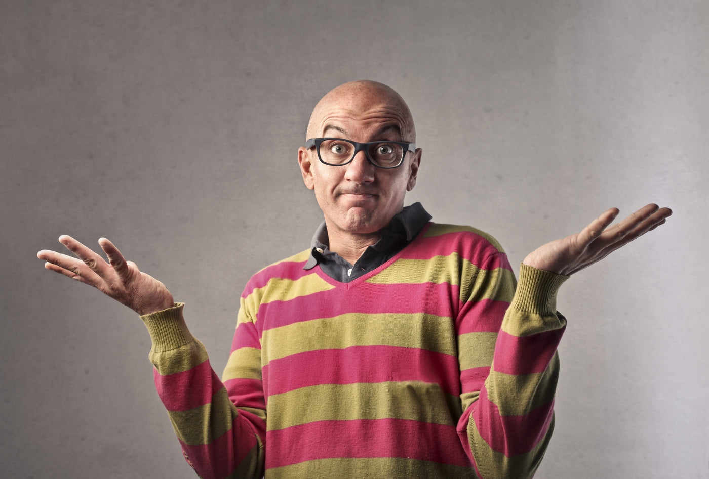 Bald man wearing glasses with his hands up implying confusion.