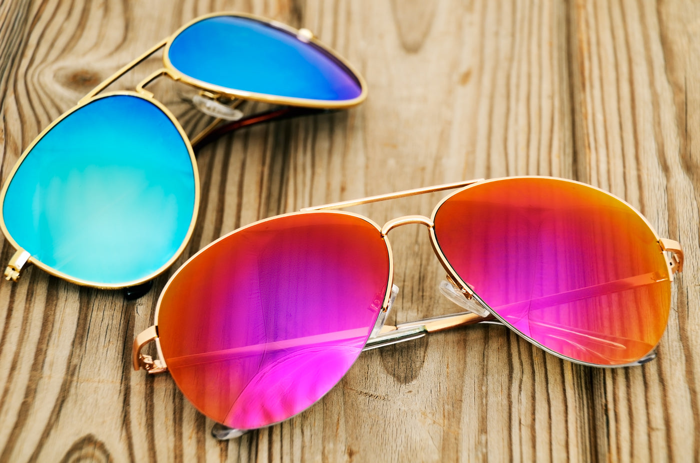Two pair of gold metal sunglasses one with blue polarized lenses and one with pink polarized lenses