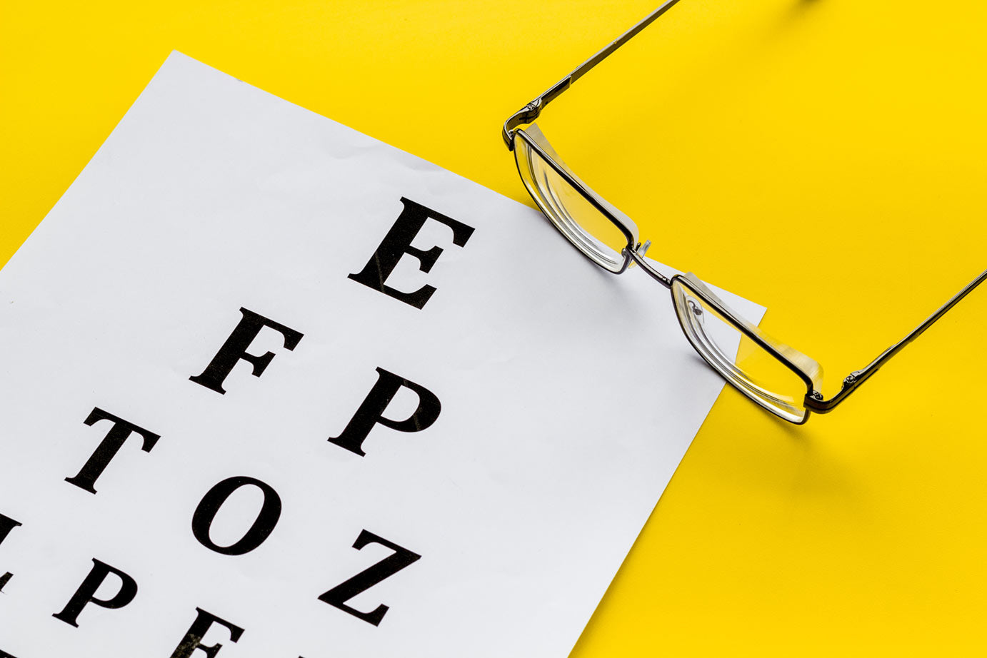 Snellen chart on yellow background with glasses laying on a table.