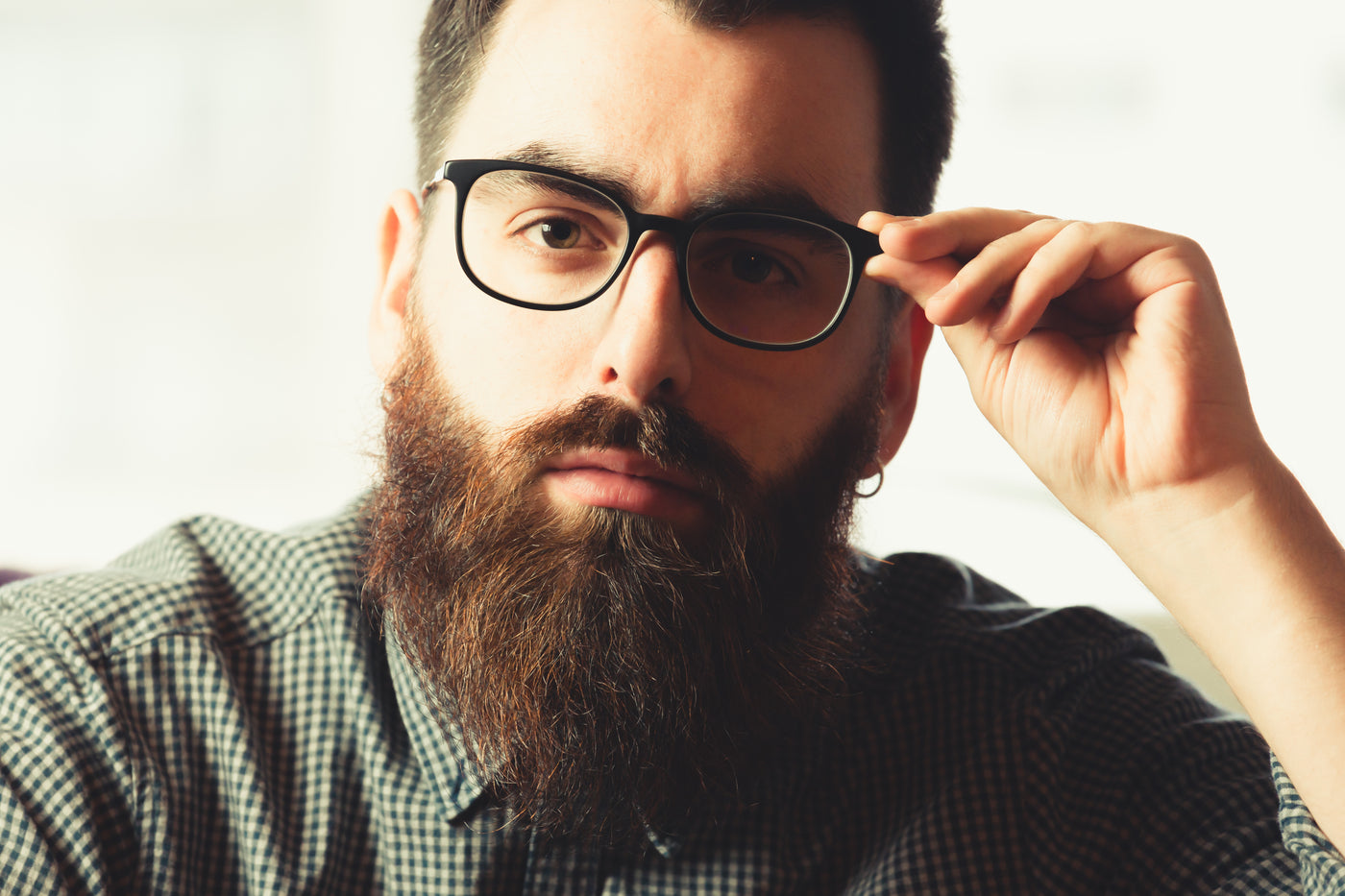 man with beard using left hand to adjust black glasses